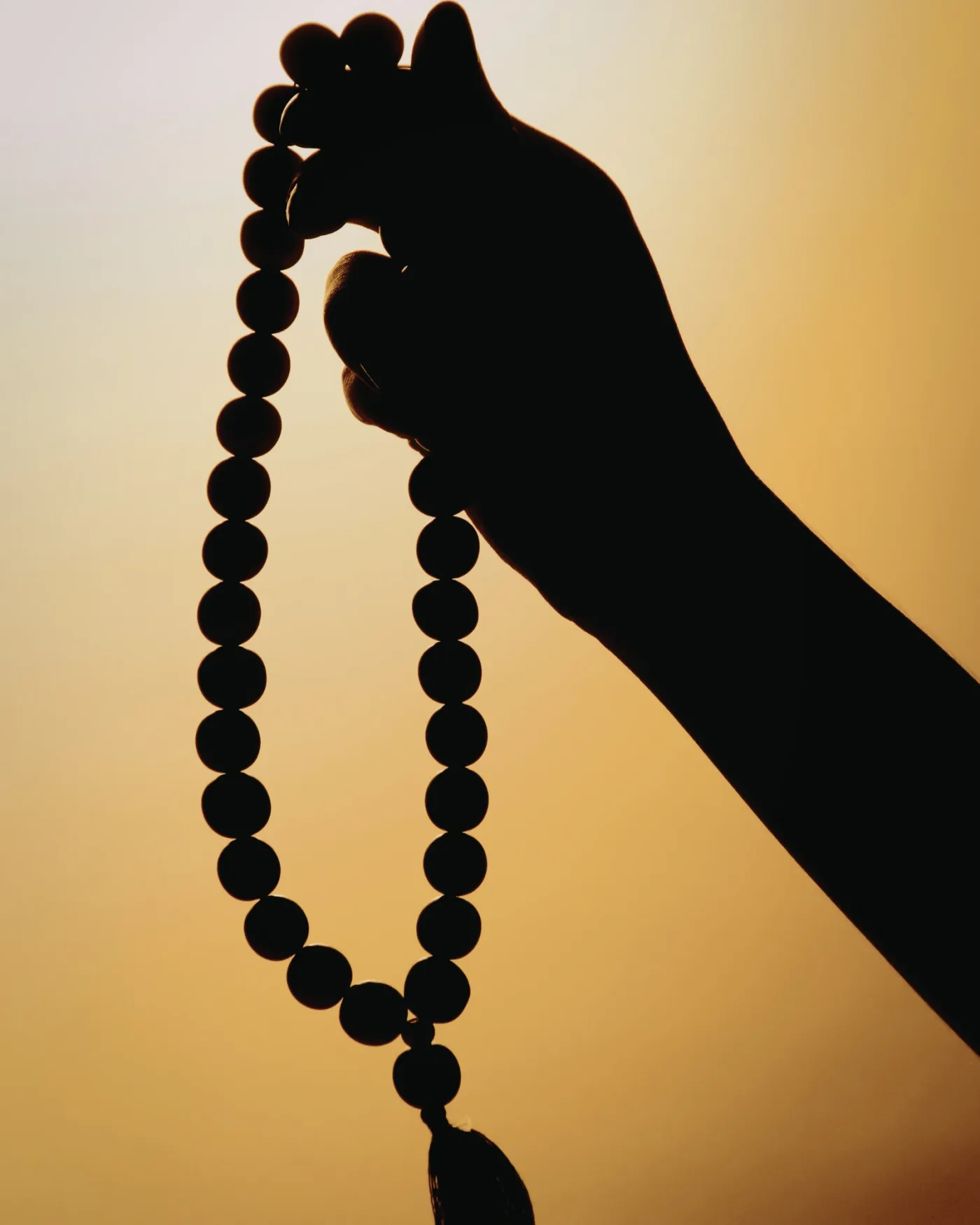 Hand holding a mala against a warm golden sky